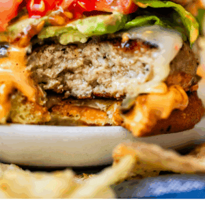 A close-up of a juicy turkey burger with lettuce, tomato, and sauce on a bun. Text at the bottom reads: “Turkey burgers you’ll actually like — The Food Charlatan.”.
