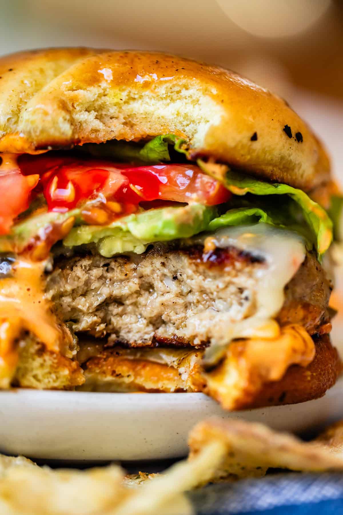 Close-up of a juicy cheeseburger with a bite taken out, showing layers of melted cheese, lettuce, tomato, creamy sauce, and a thick beef patty inside a golden toasted bun.