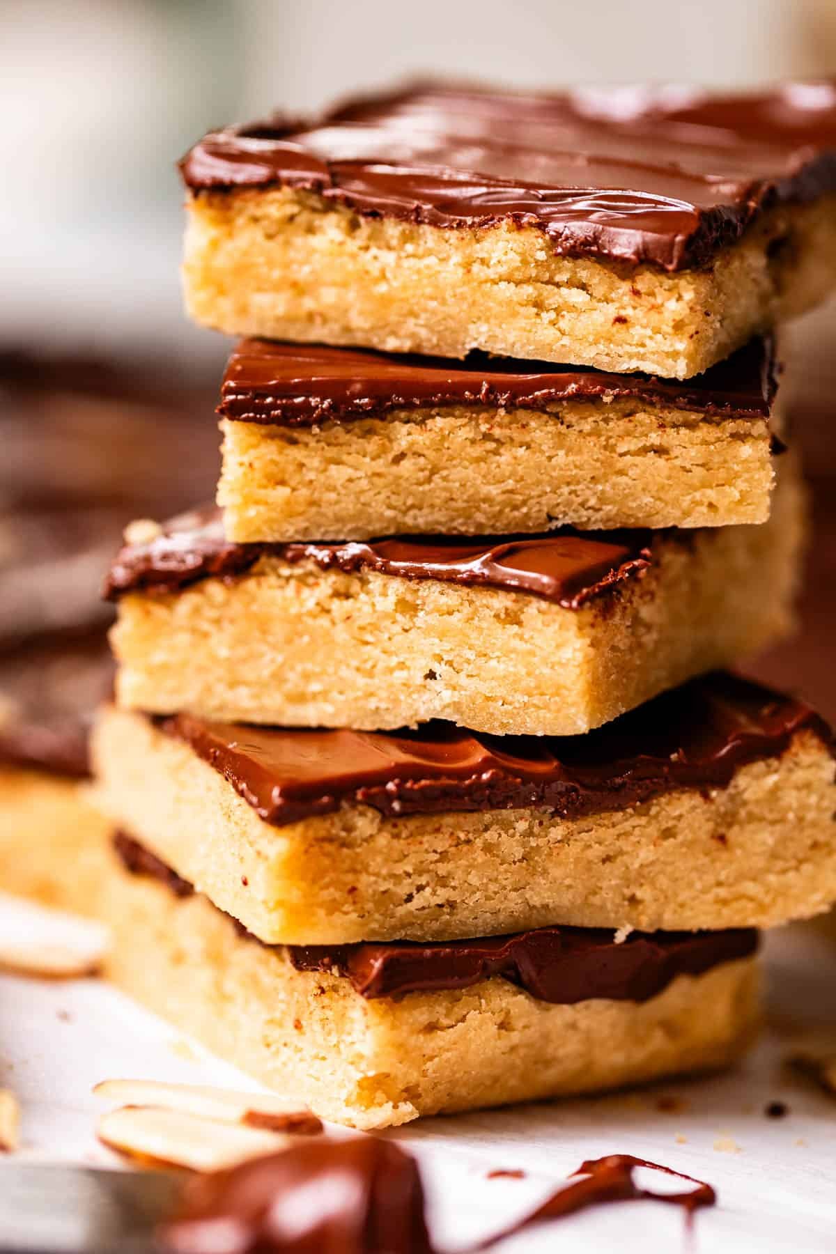 A close-up of four thick, rectangular cookie bars stacked on top of each other, each topped with a layer of melted chocolate. The bars have a golden, crumbly texture.