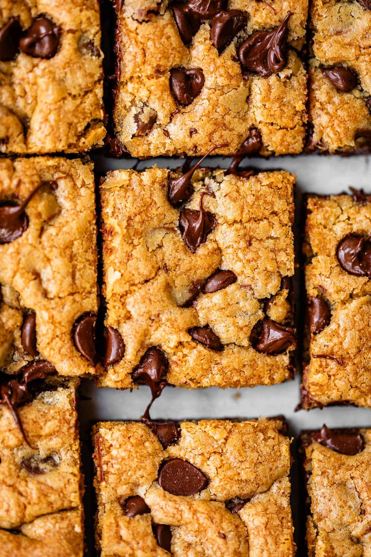 Close-up of several chocolate chip blondie bars cut into squares, showing a golden-brown, slightly crumbly texture with melted chocolate chips on top.