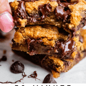 A close-up of a hand picking up a gooey, chocolatey chocolate chip cookie bar from a stack, with melted chocolate and cookie pieces visible. Text below reads: 30-Minute Chocolate Chip Cookie Bars - The Food Charlatan.