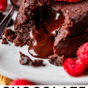 A chocolate lava cake with melted chocolate oozing out, topped with a fresh strawberry. Sliced open on a white plate with a spoon and more strawberries in the background. Text reads Chocolate Lava Cake.