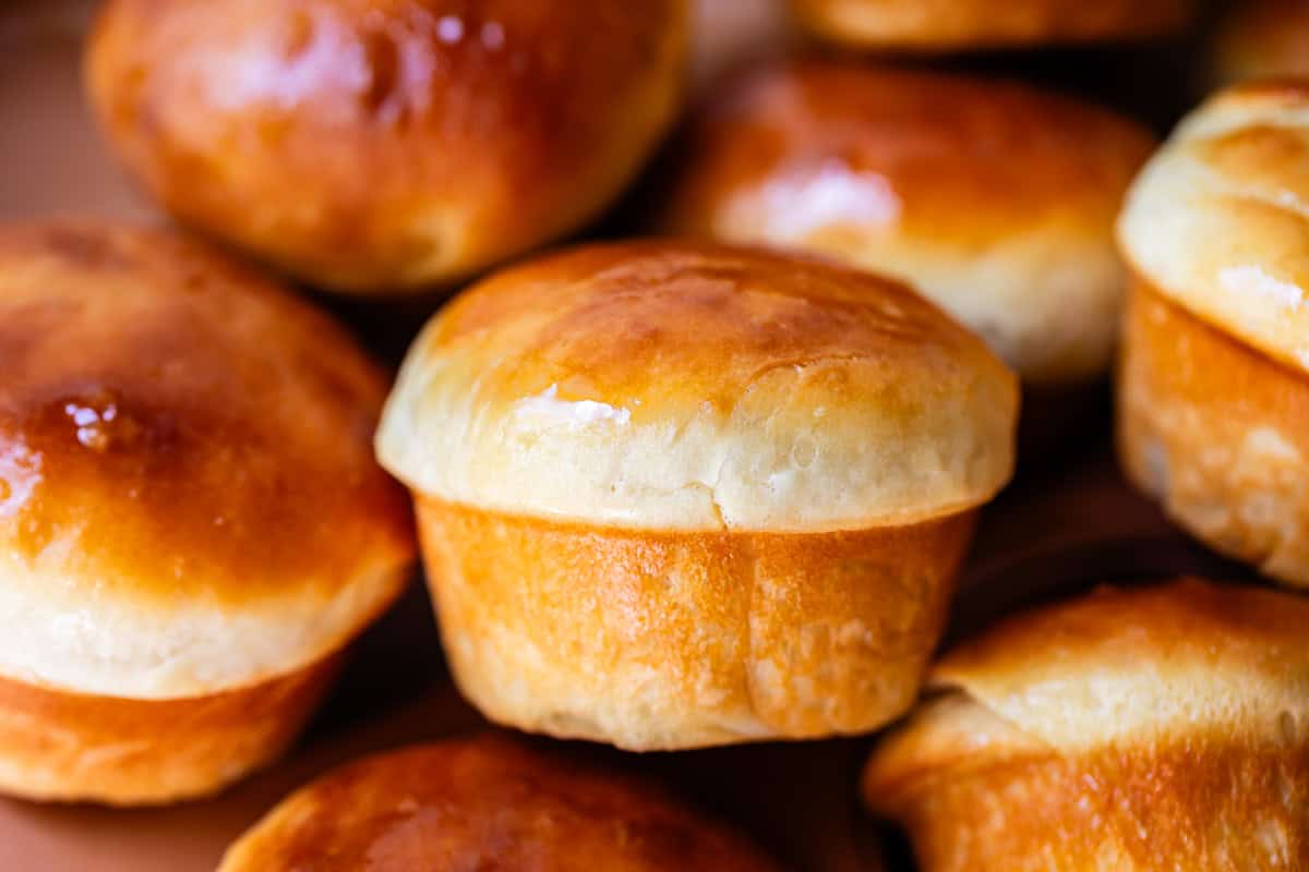 A close-up of several golden-brown, freshly baked bread rolls with shiny, glazed tops, arranged closely together.