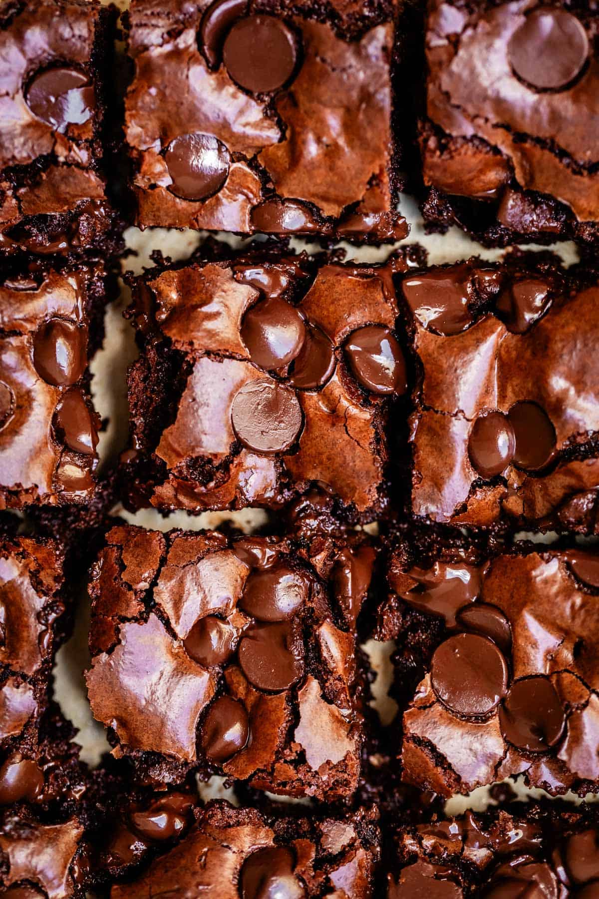Close-up of freshly baked, fudgy chocolate brownies cut into squares, topped with shiny melted chocolate chips and a crinkly, crackled surface.