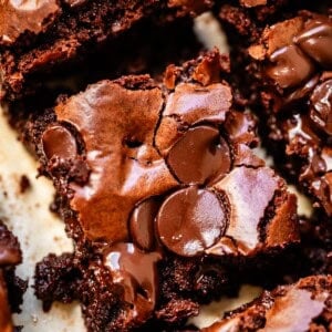 Close-up of rich, fudgy brownies topped with melted chocolate chips, showing a cracked, shiny surface and gooey, moist texture inside.