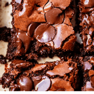 A close-up of sliced dark chocolate brownies with shiny, crackled tops and chocolate chips, arranged on a light surface. Bold text at the bottom reads Dark Chocolate Brownies and The Food Charlatan.