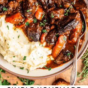 A bowl of Irish beef stew with chunks of beef, carrots, and rich gravy, served alongside mashed potatoes and garnished with fresh herbs. Slices of bread are placed on the side. Text reads: Simple Homemade Irish Beef Stew.