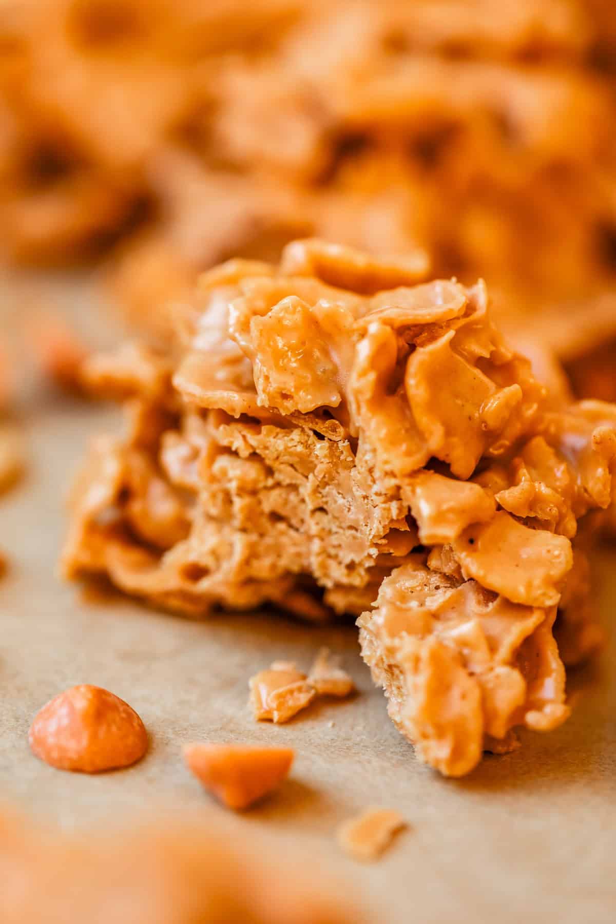 A close-up of a no-bake butterscotch haystack treat, made with crunchy chow mein noodles and coated in a creamy butterscotch mixture. Some pieces and butterscotch chips are visible on a light surface.