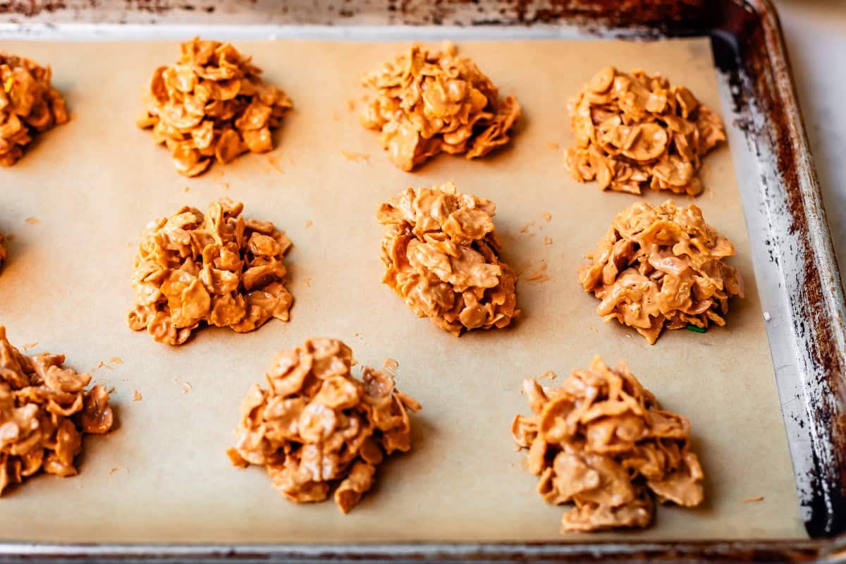Clusters of unbaked cornflake cookies are arranged on a parchment-lined baking sheet, ready to be baked.
