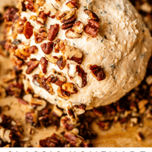 A round cheese ball coated with chopped pecans sits on a wooden surface, with fresh herbs in the background. Text reads: Classic Homemade Cheese Ball - The Food Charlatan.