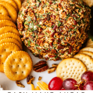 A cheese ball coated with chopped pecans and herbs, surrounded by round crackers, rectangular crackers, grapes, and a wedge of cheese on a platter. Text overlay reads: Easy Make Ahead Cheese Ball The Food Charlatan.