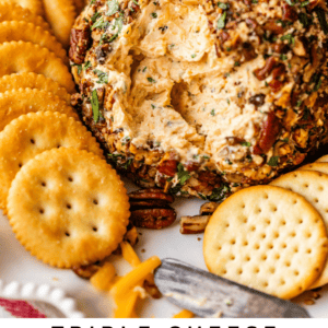 A round cheese ball coated with chopped herbs and pecans is surrounded by assorted crackers on a platter. The text at the bottom reads Triple Cheese Cheese Ball - The Food Charlatan.