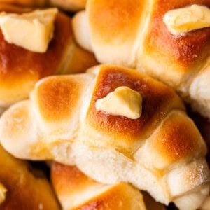 Golden brown crescent rolls topped with melting pats of butter, stacked closely together and showing a soft, fluffy texture.