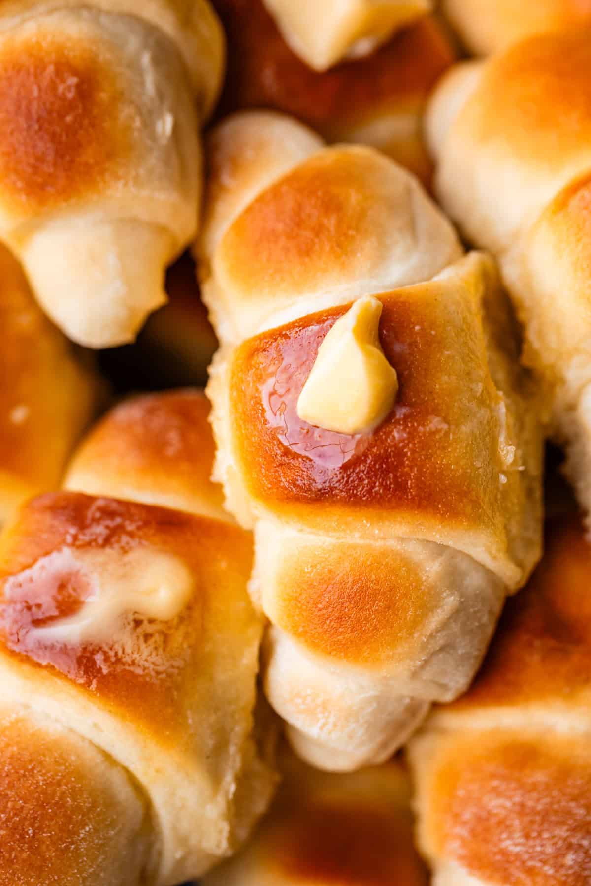 Golden-brown crescent rolls with melted butter on top, closely stacked together, showcasing their soft, fluffy texture and slightly shiny, glazed surface.
