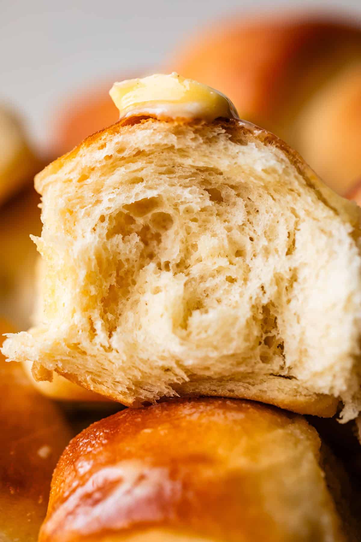 A close-up of a soft, fluffy dinner roll with a pat of melting butter on top, showing its airy, tender interior.