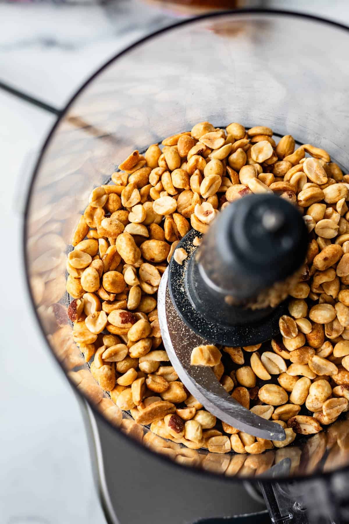 A close-up view of a food processor filled with roasted peanuts, ready to be blended.