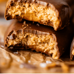 Close-up of two chocolate-covered Reeses eggs stacked, with bites taken out to reveal a crumbly peanut butter filling. Text at the bottom reads: Reeses Eggs - That Crumbly Texture - The Food Charlatan.