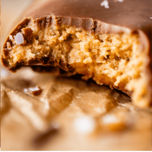 A close-up of a Reese’s Eggs chocolate candy with a bite taken out, showing its crumbly peanut butter filling. The text at the bottom reads, REESES EGGS *That crumbly texture* The Food Charlatan.