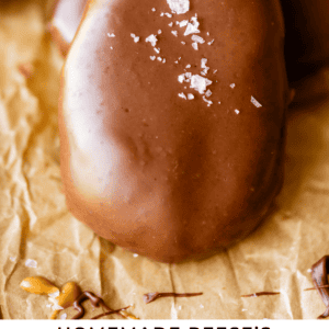 A homemade chocolate-covered peanut butter egg sprinkled with flaky sea salt sits on parchment paper. Text at the bottom reads: Homemade Reeses Peanut Butter Eggs - The Food Charlatan.