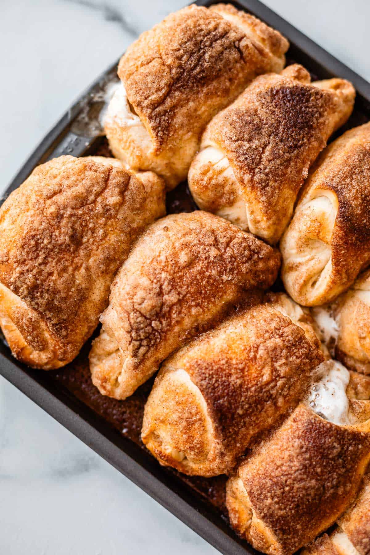 A tray filled with freshly baked crescent rolls topped with golden brown cinnamon sugar, some with melted filling visible at the edges.