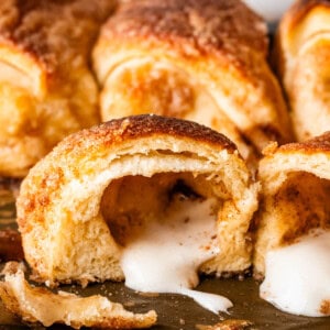 Close-up of golden-brown resurrection crescent rolls, with one roll cut open to reveal a gooey, melted marshmallow filling oozing out onto the baking sheet.
