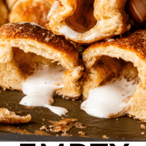 A hand lifts a cinnamon-sugar coated roll with a hollow center and melted marshmallow inside. Other similar rolls are on a tray, some split open to show their empty centers. Text reads EMPTY TOMB ROLLS.