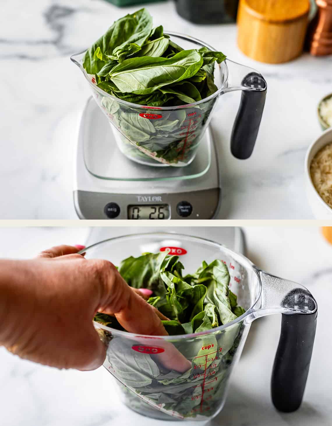 A clear measuring cup filled with fresh basil leaves sits on a kitchen scale reading 2.6 oz. In the second image, a hand presses down on the basil leaves in the cup. Marble countertop and kitchen items are visible in the background.