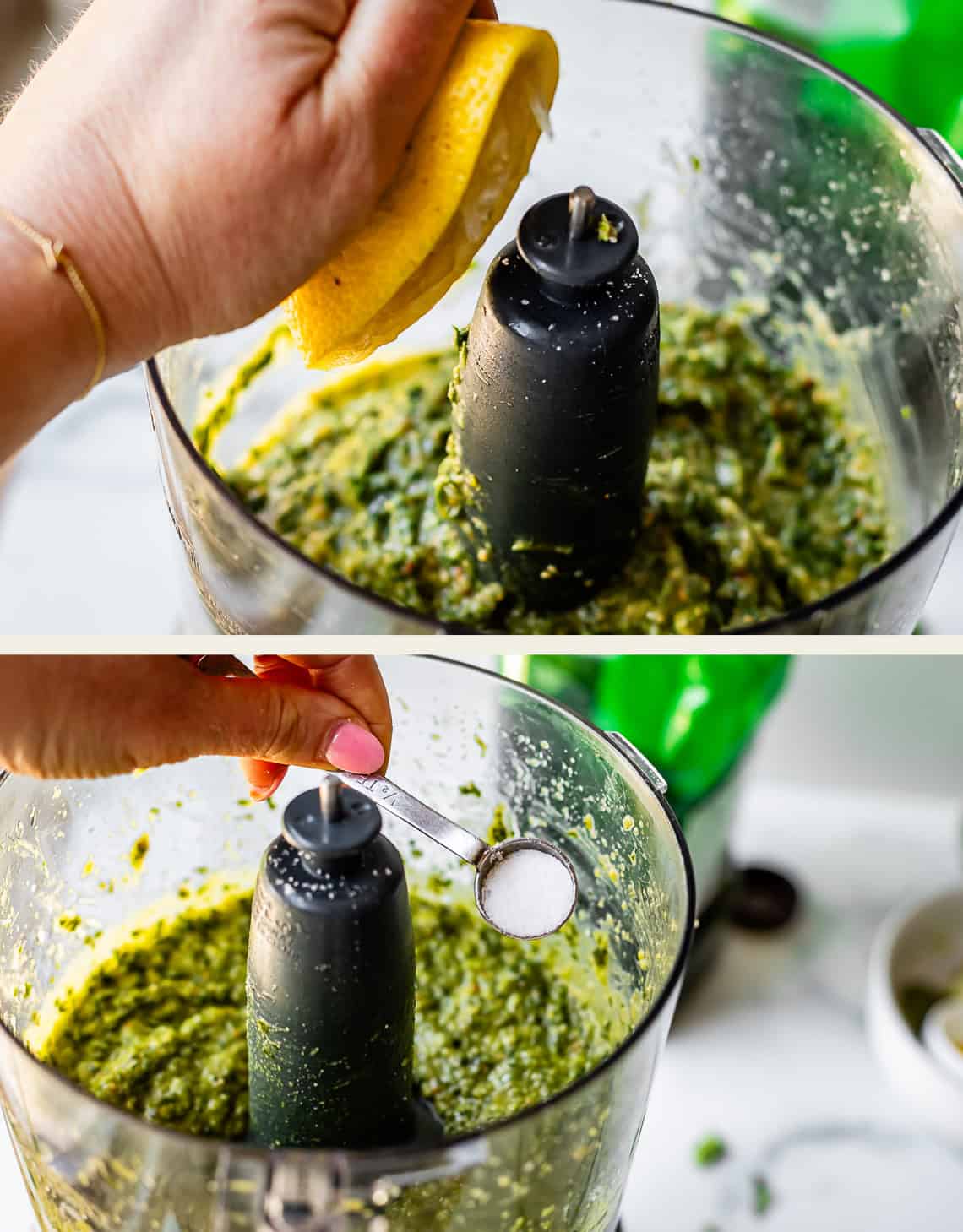 A person squeezes a lemon half and adds a spoonful of salt to a green mixture in a food processor, preparing a sauce or pesto.