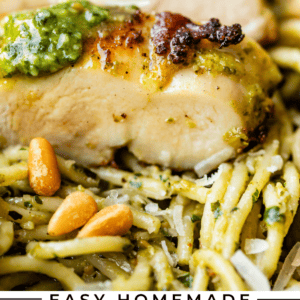 Close-up of sliced chicken breast topped with green pesto sauce and served over spaghetti noodles, garnished with pine nuts and shredded cheese. Text below reads: Easy Homemade Pesto Chicken - The Food Charlatan.
