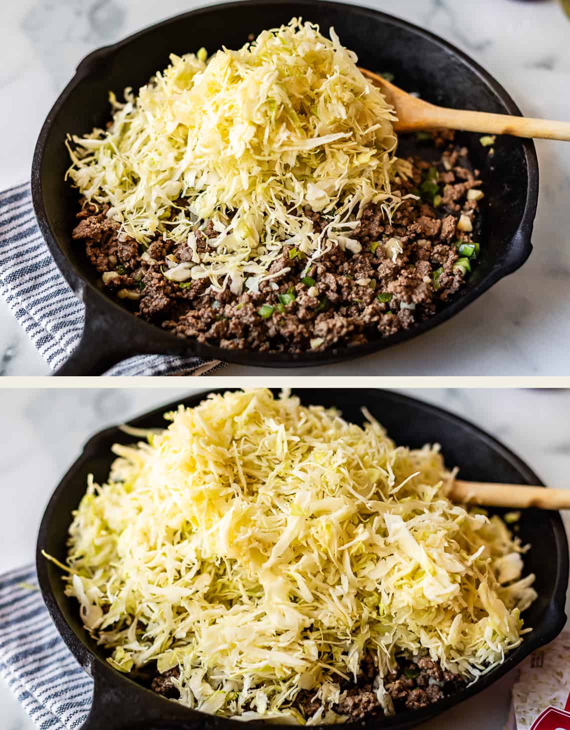 A black skillet filled with cooked ground meat and chopped green vegetables, topped with a large mound of shredded cabbage, sits on a striped towel with a wooden spoon on the side.