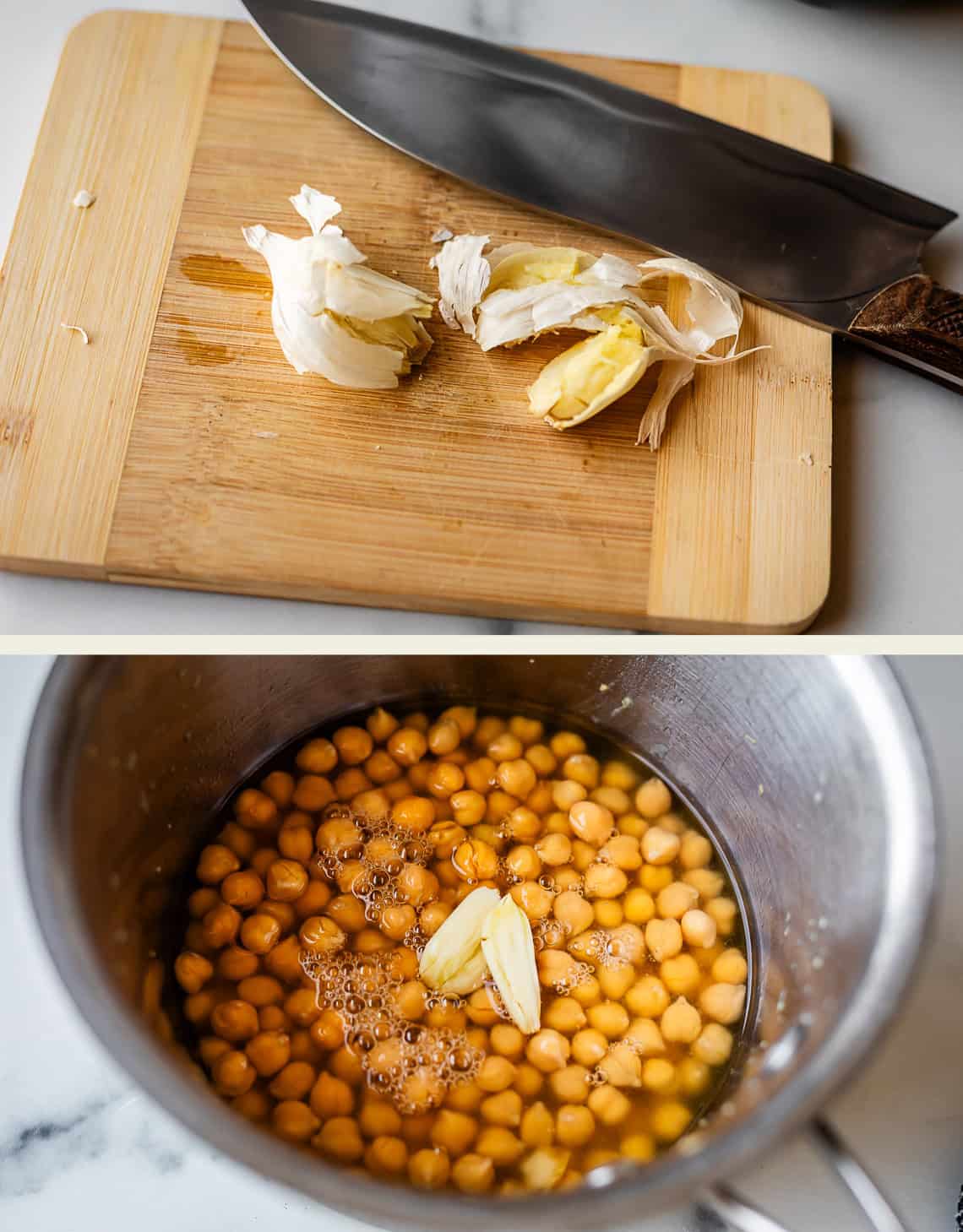 A cutting board with smashed garlic cloves and a knife, above a pot containing chickpeas, water, and pieces of garlic on a marble countertop.