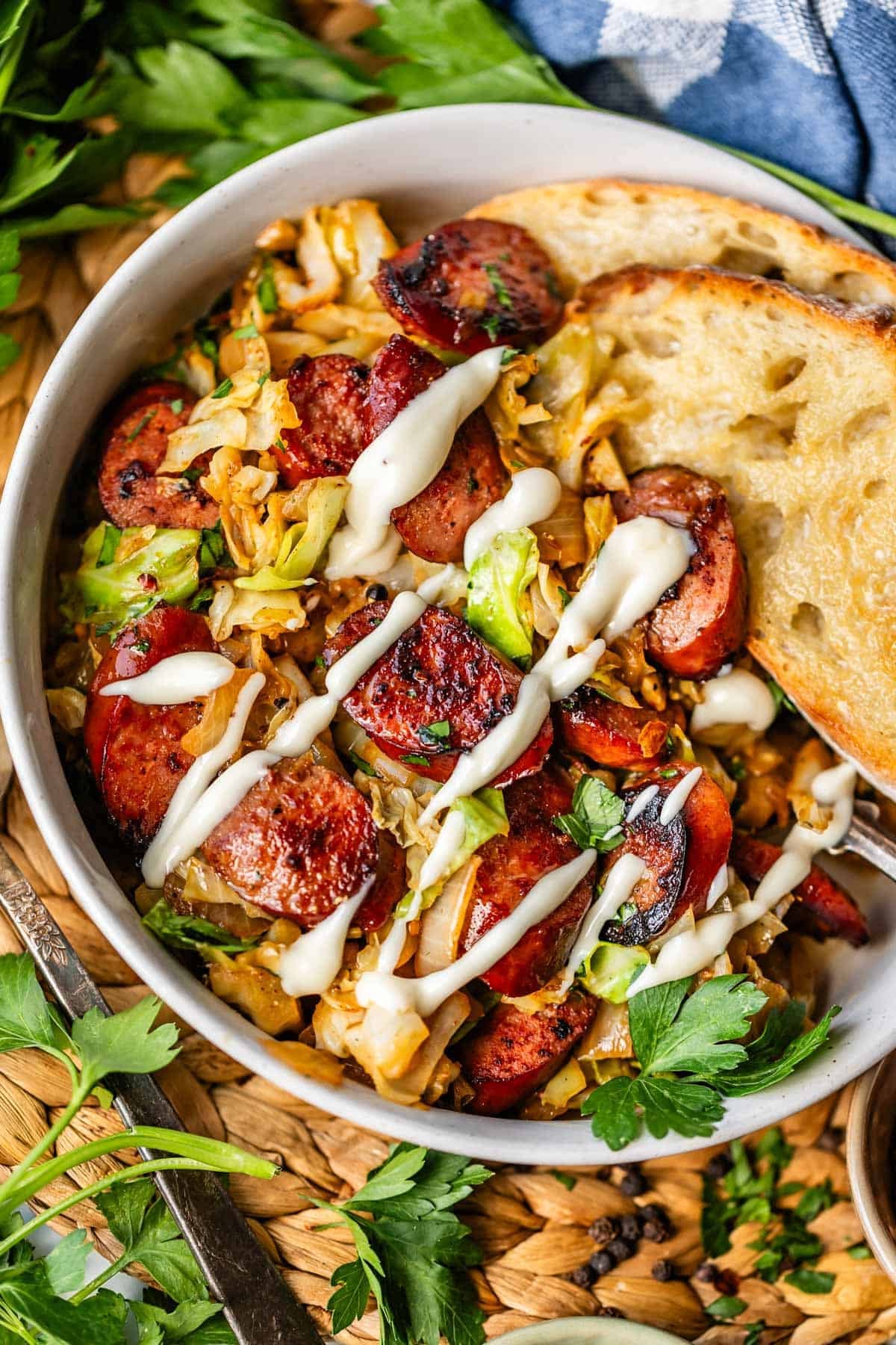 A bowl of saut&eacute;ed cabbage and sliced sausage, topped with a drizzle of creamy white sauce, served with two slices of toasted bread and garnished with fresh parsley.