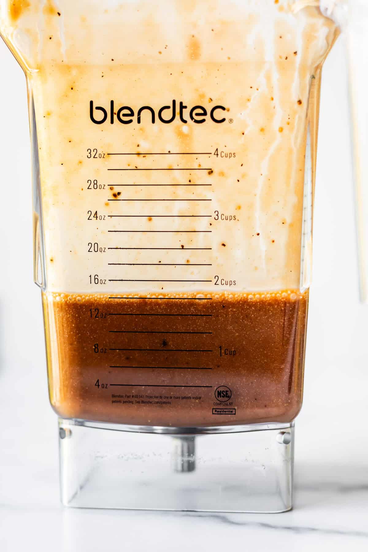 A close-up of a Blendtec blender jar with a creamy light mixture on top and a brown liquid settling at the bottom, showing measurement markings up to 32 ounces and 4 cups.