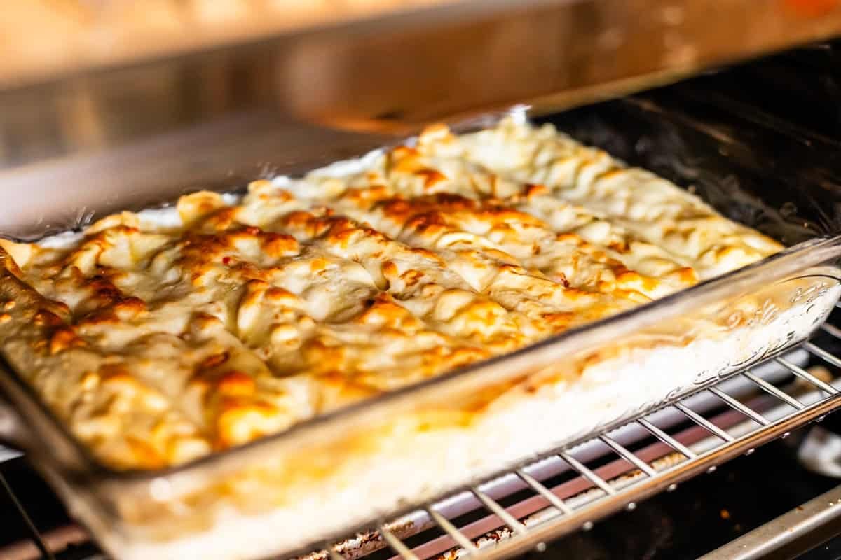 A glass baking dish filled with golden-brown, cheesy baked lasagna sits on an oven rack, bubbling and hot under the broiler.