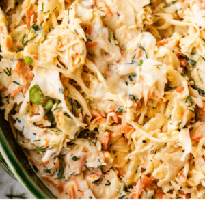 Close-up of a bowl filled with creamy coleslaw made of shredded cabbage, carrots, and herbs, with a spoon inside. Text at the bottom reads Easy Coleslaw Recipe - The Food Charlatan.