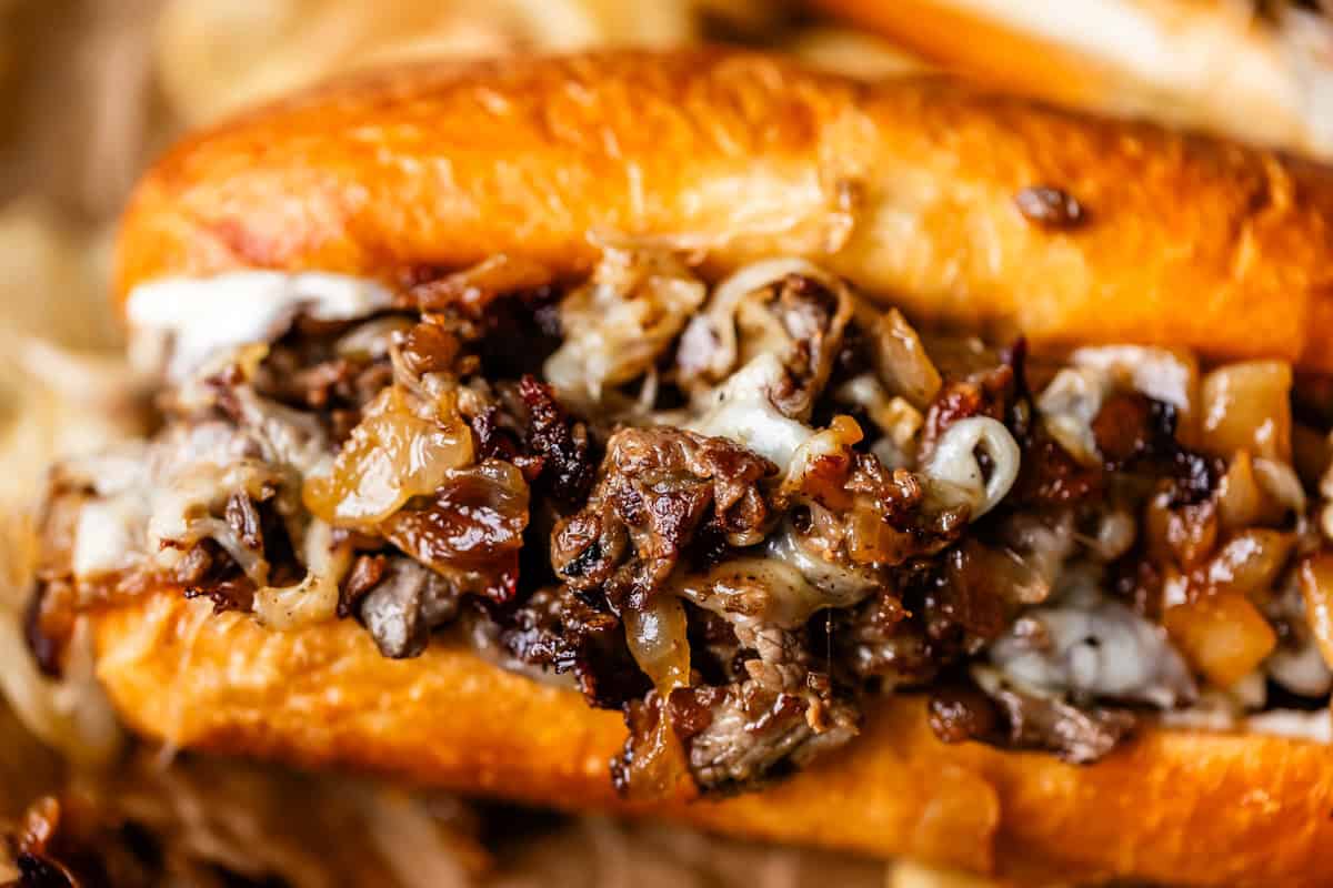 Close-up of a Philly cheesesteak sandwich filled with sliced beef, melted cheese, and saut&eacute;ed onions in a toasted hoagie roll.