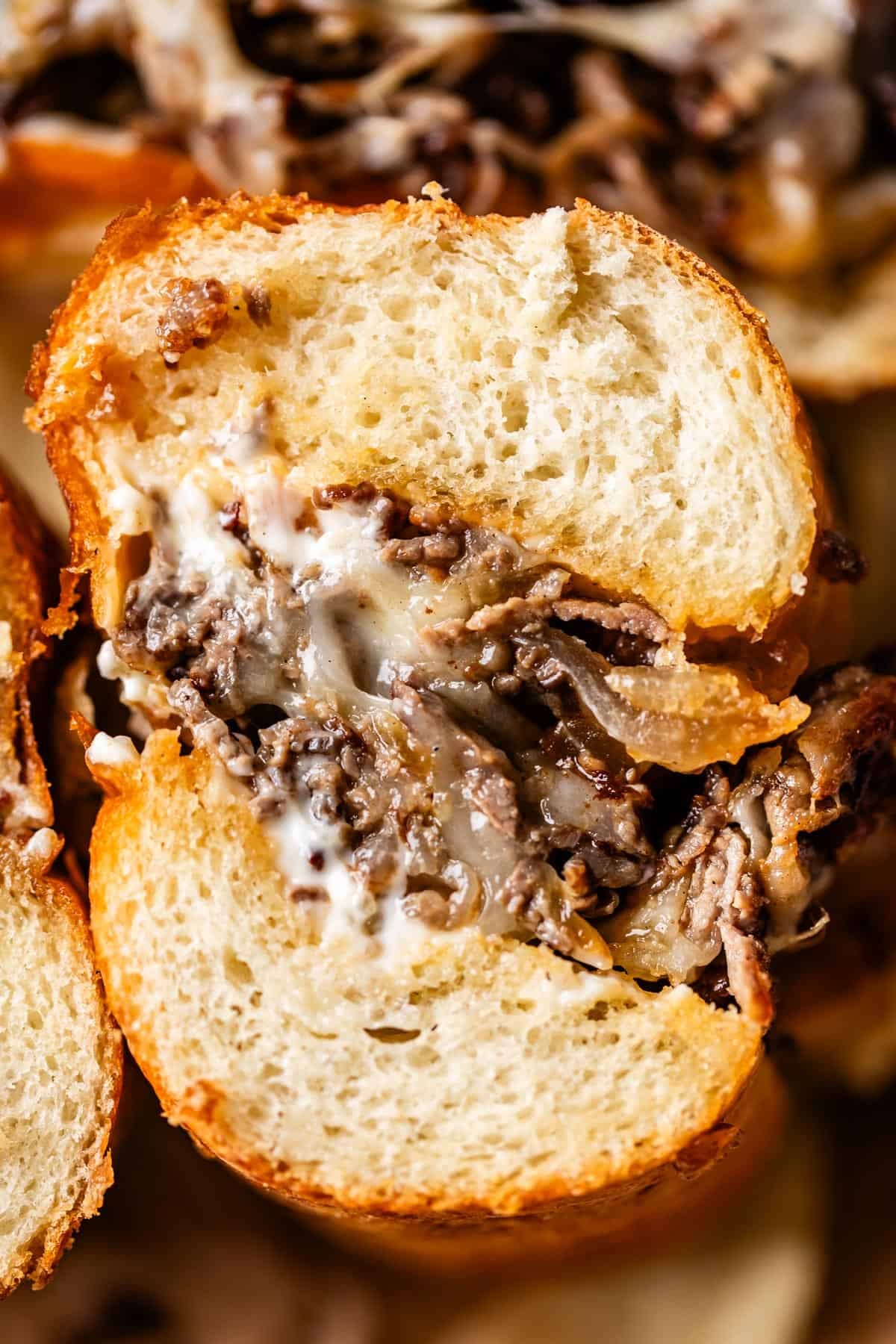 A close-up of a sandwich with golden, crusty bread filled with melted cheese, thinly sliced beef, and creamy sauce.