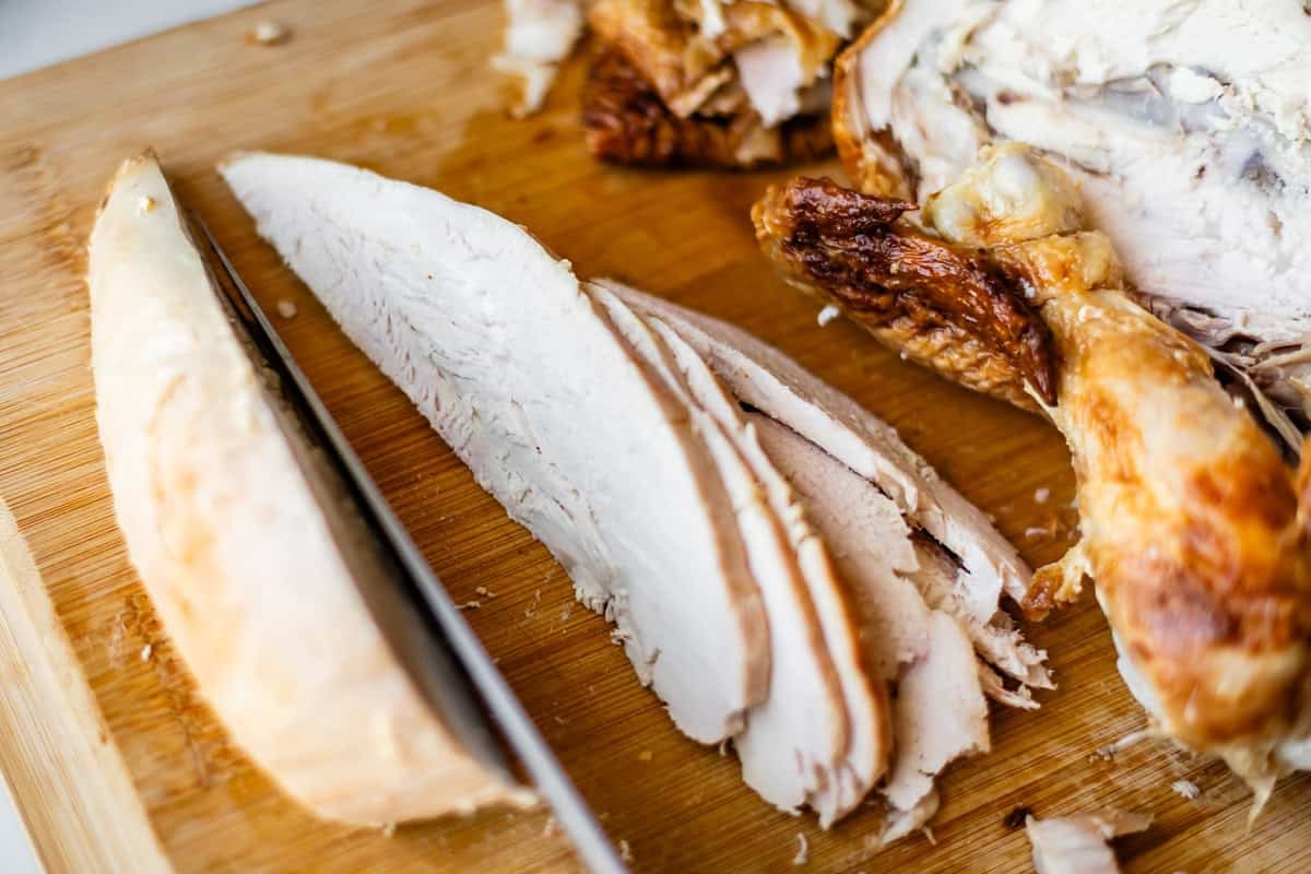 Sliced roasted turkey breast on a wooden cutting board with a knife, showing juicy white meat and crispy brown skin.