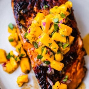 Grilled salmon fillet topped with a vibrant mango salsa, garnished with fresh herbs, served on a white plate.