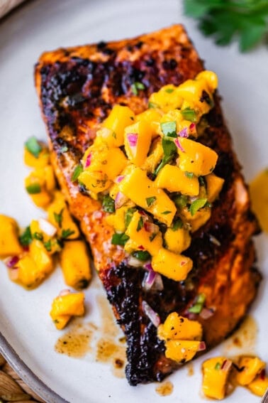 Grilled salmon fillet topped with a vibrant mango salsa, garnished with fresh herbs, served on a white plate.