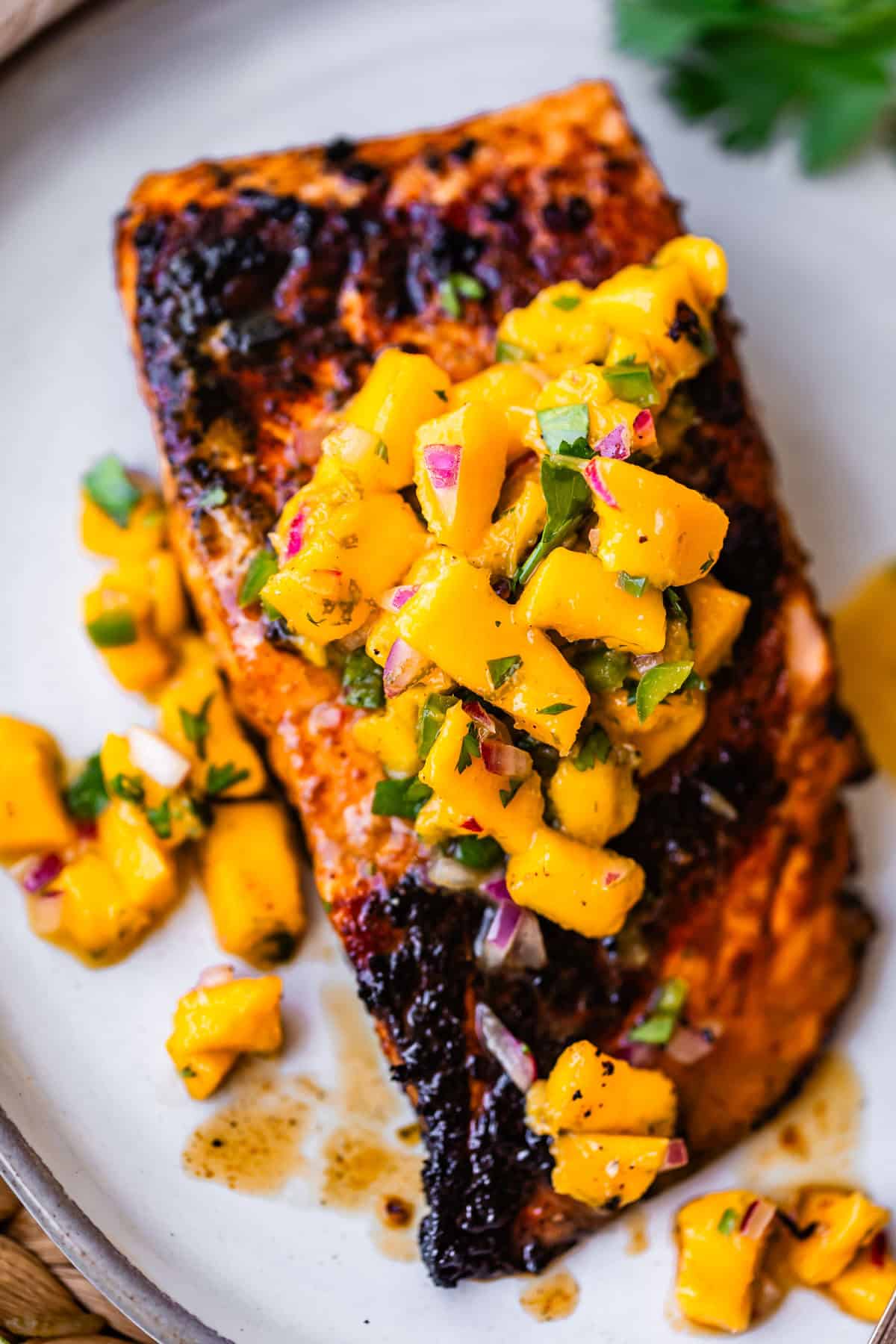 Grilled salmon fillet topped with a vibrant mango salsa, garnished with fresh herbs, served on a white plate.