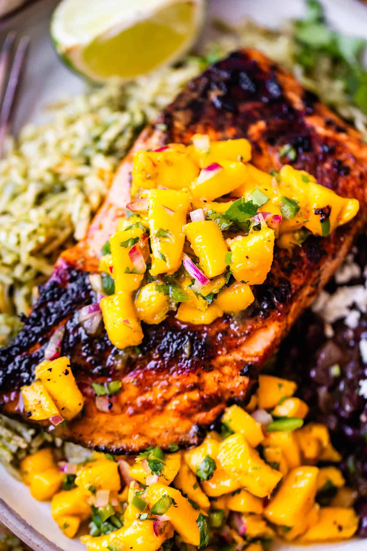 Grilled salmon topped with mango salsa, served with green rice and black beans. A lime wedge is in the background.