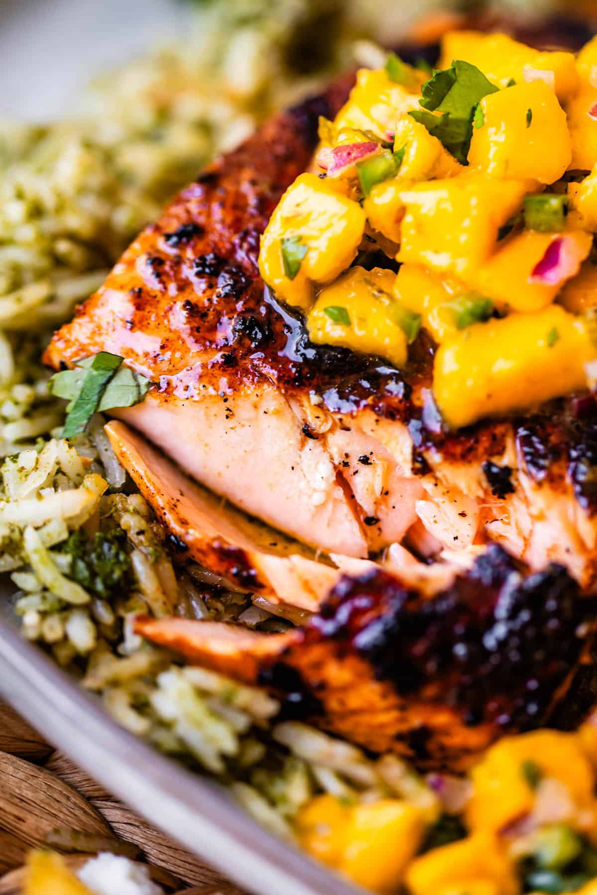 Grilled salmon fillet topped with mango salsa, served on a bed of herbed rice. The dish is garnished with chopped cilantro and red onion.