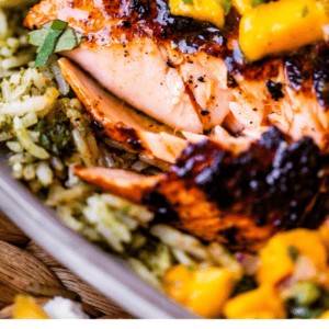 Close-up of blackened salmon served on a bed of rice, topped with a bright mango salsa, with text at the bottom reading Easy Homemade Blackened Salmon – The Food Charlatan..