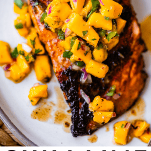 A plate with a piece of chili lime blackened salmon topped with vibrant mango salsa, garnished with herbs. Text at the bottom reads: Chili Lime Blackened Salmon with Mango Salsa..