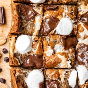 A close-up of smores bars cut into squares, topped with melted chocolate pieces and toasted marshmallows on a wooden surface.