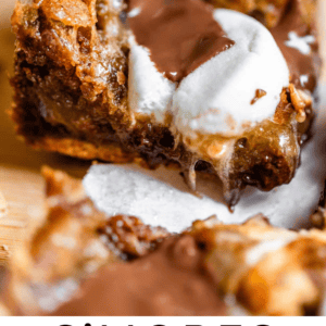 A close-up of gooey smores cookie bars with melted chocolate and marshmallow oozing out, sitting on parchment paper. Text at the bottom reads Smores Cookie Bars, The Food Charlatan..