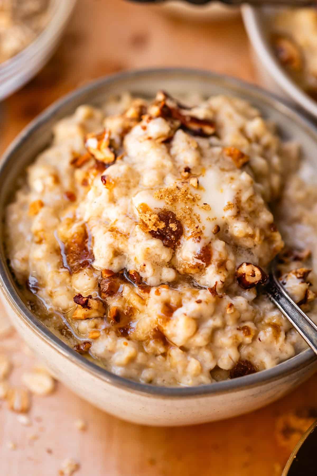 A bowl of oatmeal topped with chopped nuts, brown sugar, and a splash of milk, with a spoon scooping some from the bowl.