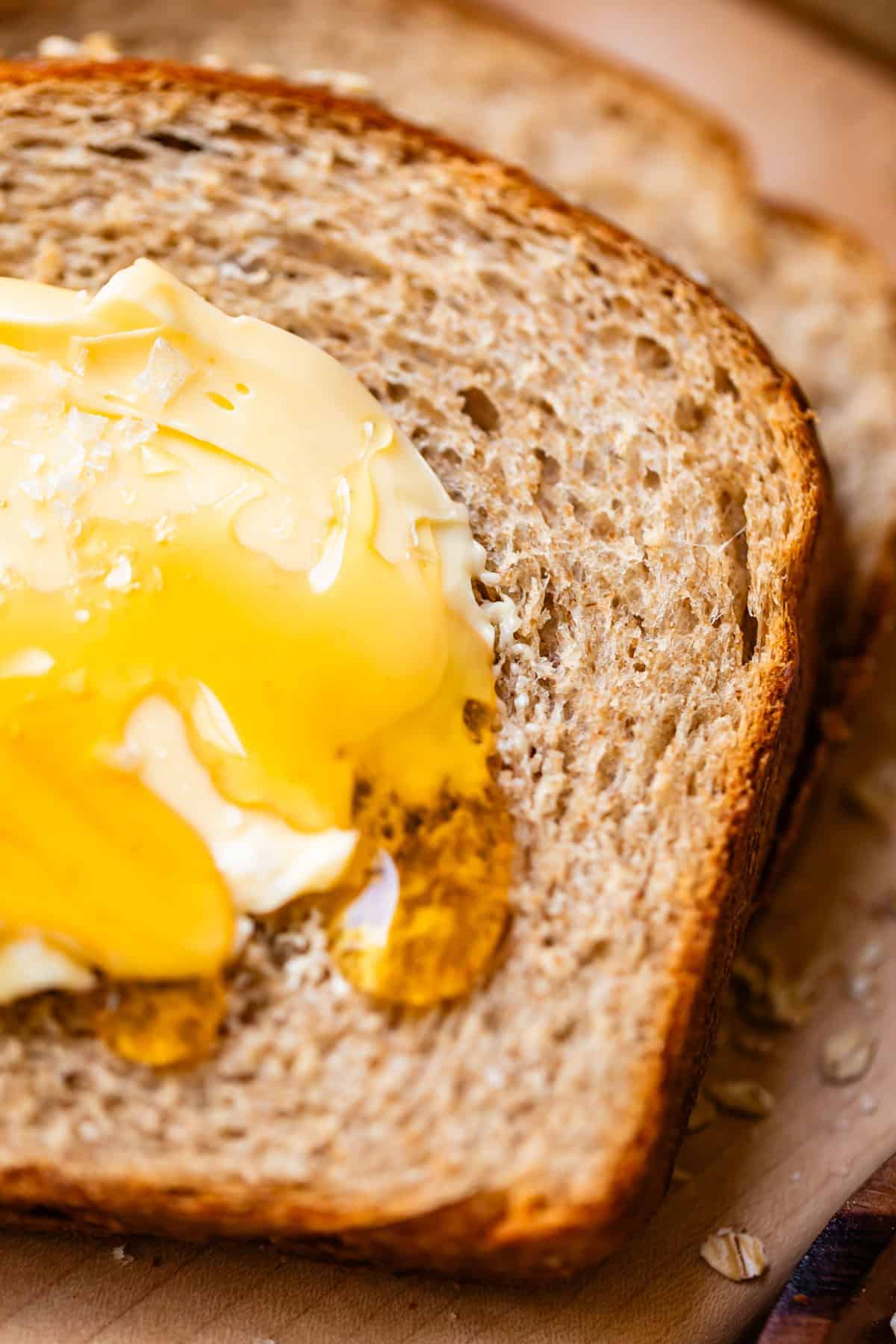 A close-up of whole wheat bread topped with a dollop of butter and drizzled honey, showing the breads texture and the melting butter blending with the honey.