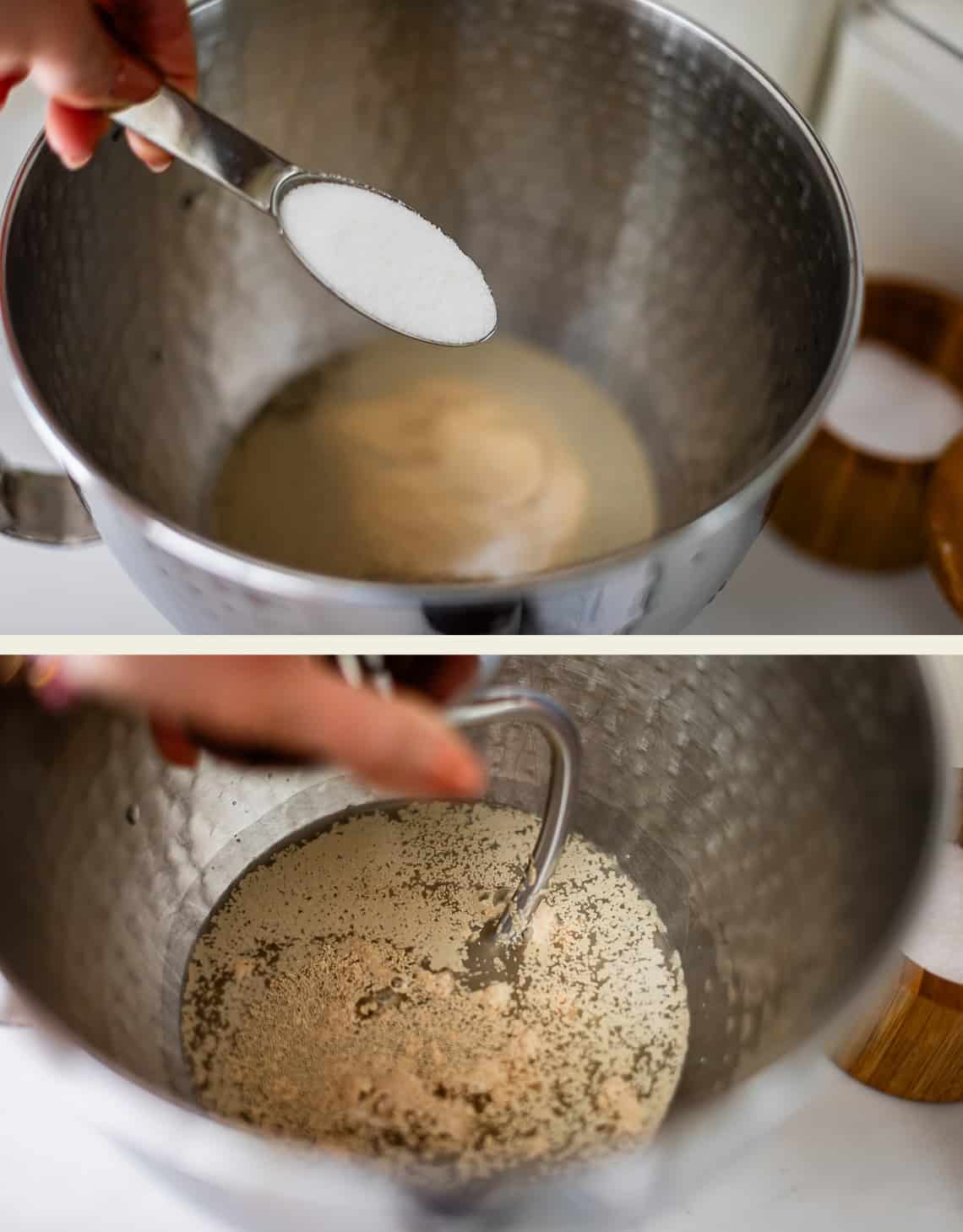 A hand pours a spoonful of white powder into a metal mixing bowl containing liquid and yeast, followed by a metal dough hook mixing the ingredients.